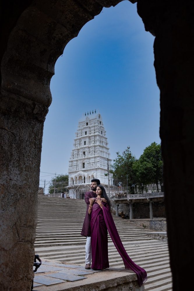 Couple framed through a heritage stone arch with a temple in the background